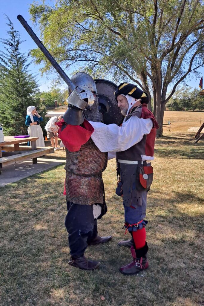 A fighter in garb having his armor checked by the Knights Marshal.