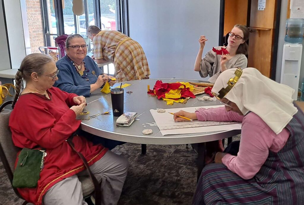 A group of people in garb sitting around a table working on crafting projects.