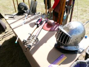 Angled view of a table covered in various different swords, shields, and pieces of armor.